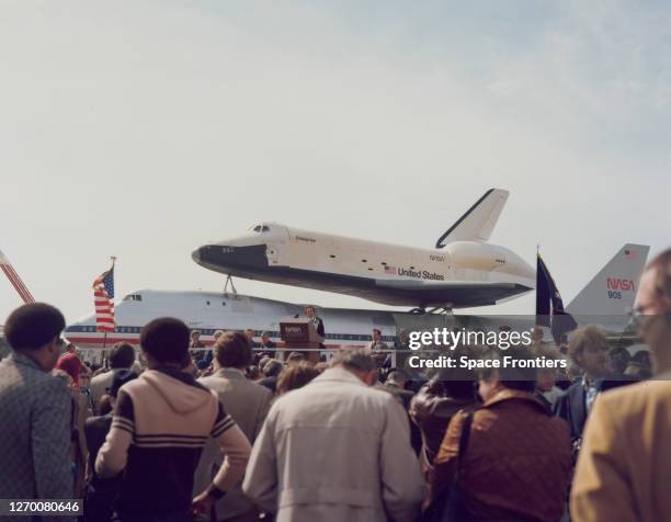 United States Congressman Ronnie Flippo addresses a crowd from a lectern with the Space Shuttle Enterprise atop NASA 905, a 747 carrier aircraft in...