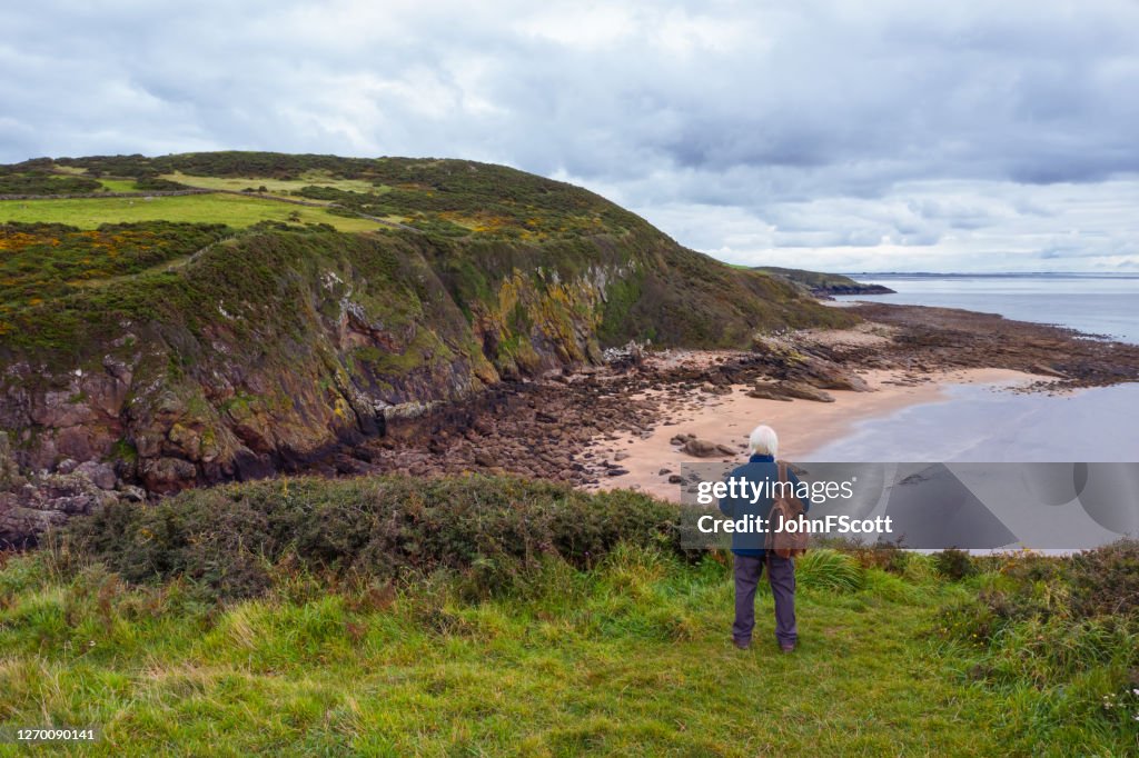 Utsikten från en drönare av en äldre man som står ensam vid kusten i Dumfries and Galloway, sydvästra Skottland