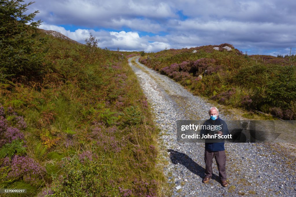 The high angle view of an active senior man wearing a face mask while standing on a dirt road in a remote part of Dumfries and Galloway, south west Scotland