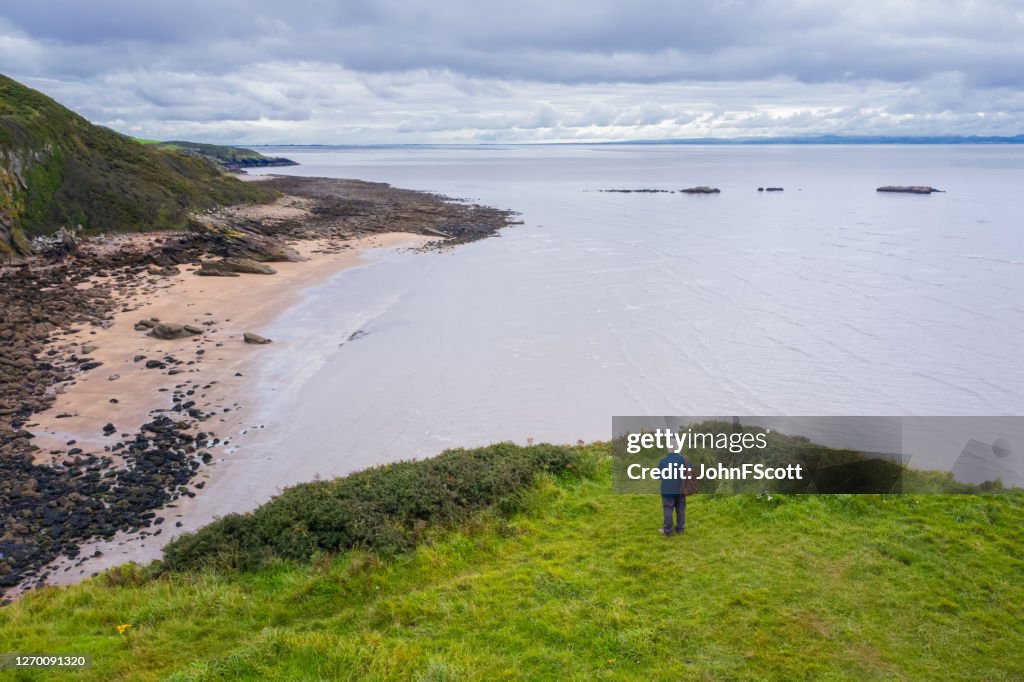 The drone view of a senior man standing alone at the coast in Dumfries and Galloway, south west Scotland