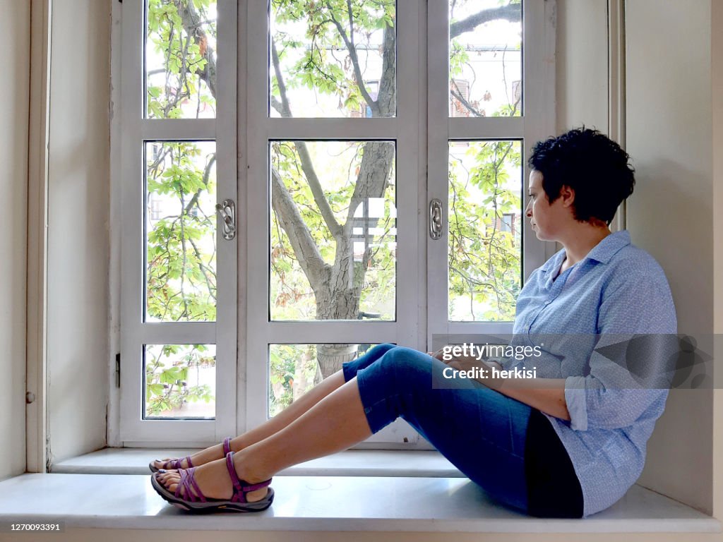 Woman wearing a protective mask is looking out of the window.