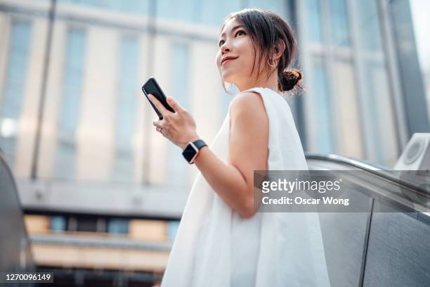 cheerful young woman holding mobile phone on escalator - 日本人　空港 ストックフォトと画像