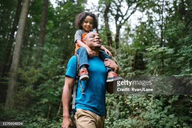 father carries son on hike through forest trail in pacific northwest - multiracial person stock pictures, royalty-free photos & images