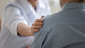 Close up caring doctor touching mature patient shoulder