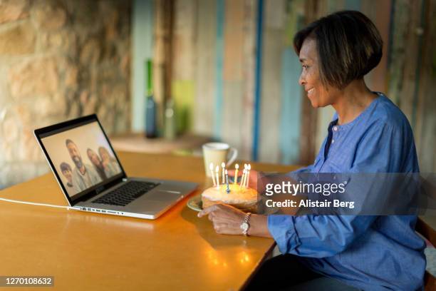mature woman blowing out birthday cake candles on a video call - older woman birthday stock pictures, royalty-free photos & images