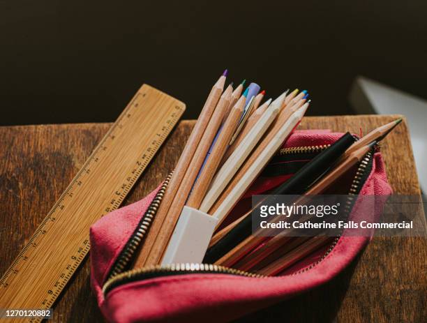 pink pencil case filled with pencils and pens on a wooden table beside a ruler. - trousse d'écolier photos et images de collection