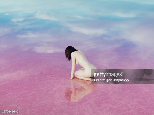 rear view of young nude woman sitting in pink lake - lake bottom foto e immagini stock