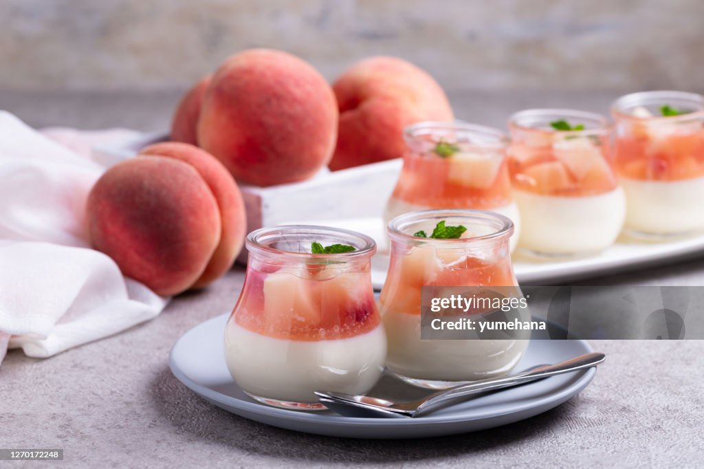 Homemade panna cotta with slices of peach and peach jelly in glass jars on a gray concrete background.