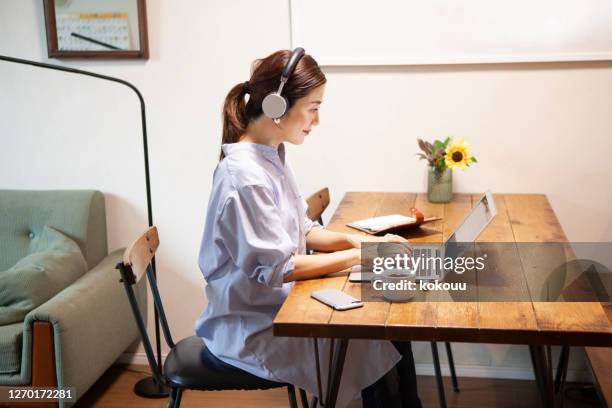 junge berufstätige mutter verwendet kopfhörer mit computer in ihrem home-office - hot desking arbeitsplatz stock-fotos und bilder