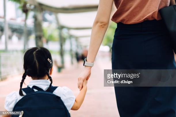 rear view of young asian mother taking her little daughter to school, they are holding hands and walking in the city street in the morning - school students uniform walking stock pictures, royalty-free photos & images