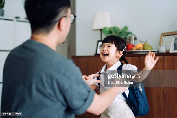 excited and happy little asian school girl getting dressed with her father in the living room and preparing for her first day at school - enfant cartable photos et images de collection