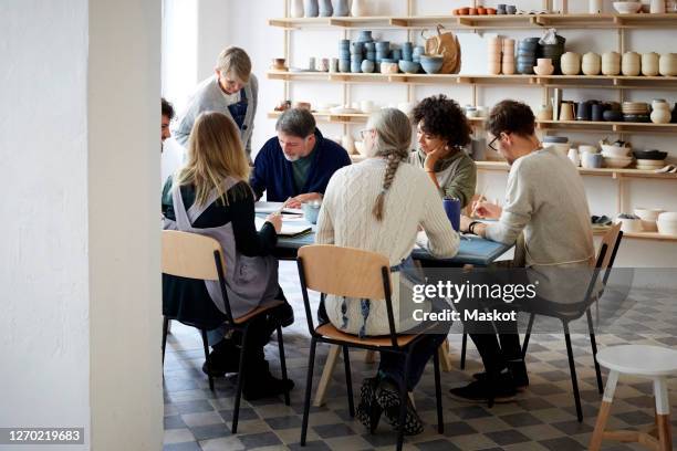 female instructor examining drawing of students at table during art class - ceramics stock pictures, royalty-free photos & images