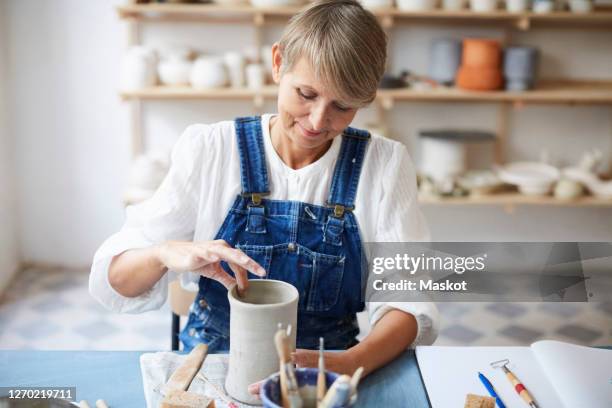 mature woman molding earthenware at table in art class - woman hobbies stock pictures, royalty-free photos & images