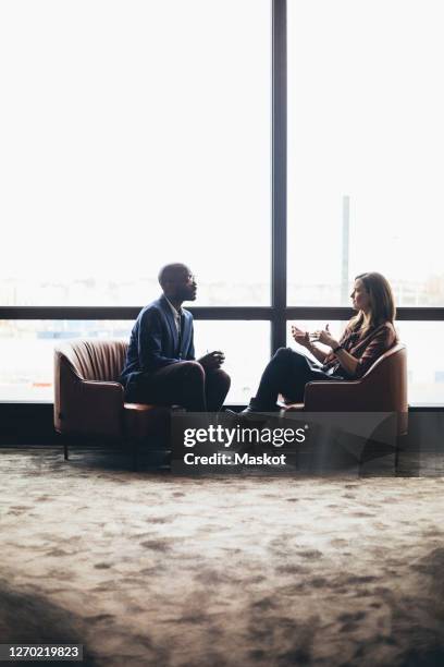 female and male coworkers discussing while sitting against window at workplace - 2 businessmen in silhouette stock pictures, royalty-free photos & images