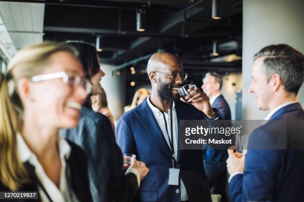 smiling entrepreneur drinking black coffee while standing with colleagues in office - sociale bijeenkomst stockfoto's en -beelden