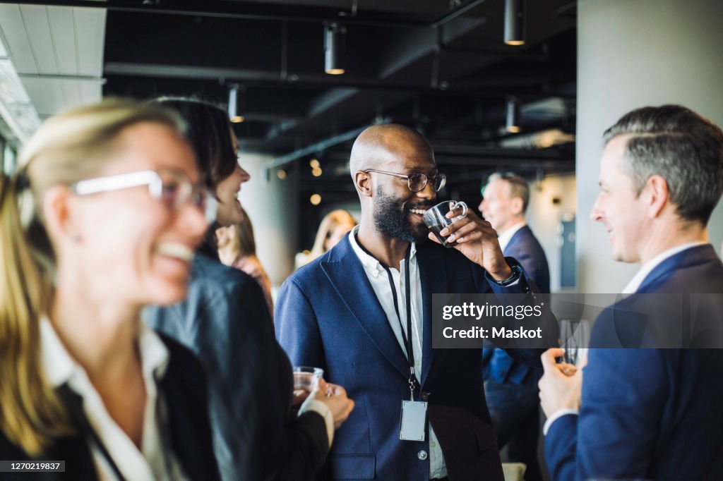 Smiling entrepreneur drinking black coffee while standing with colleagues in office