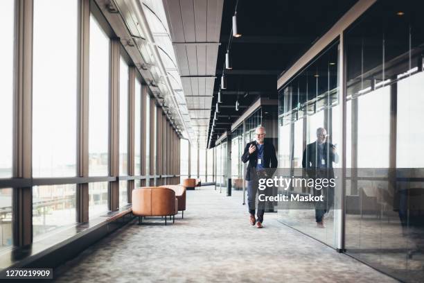 mature businessman using smart phone while walking in corridor at workplace - office hallway stock pictures, royalty-free photos & images