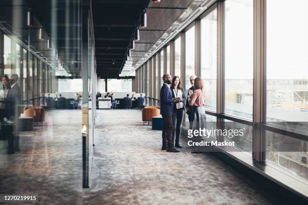business colleagues discussing while standing in office corridor - small group of people stock-fotos und bilder