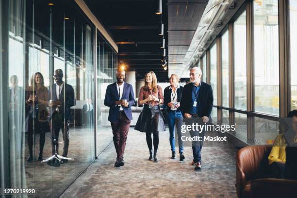 smiling female and male colleagues walking in corridor at workplace - congress meeting stock pictures, royalty-free photos & images