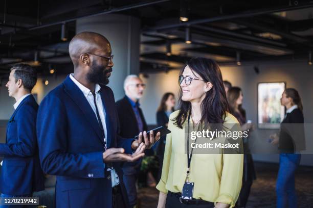 side view of smiling male with smart phone talking to female colleague in office - congress meeting stock pictures, royalty-free photos & images