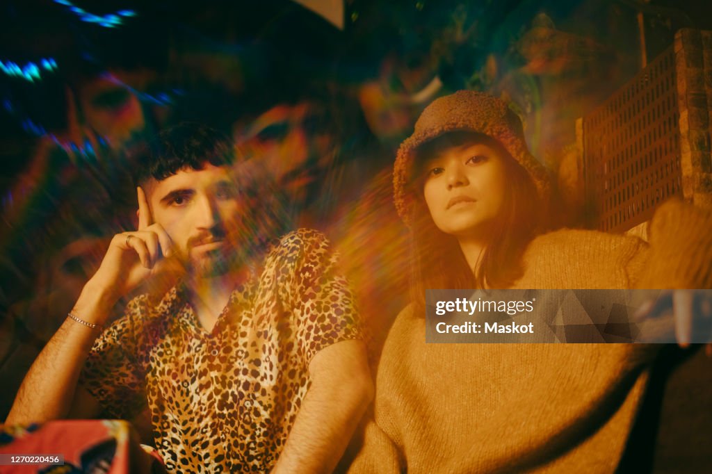 Multiple exposure of young male and female friends sitting together at illuminated restaurant