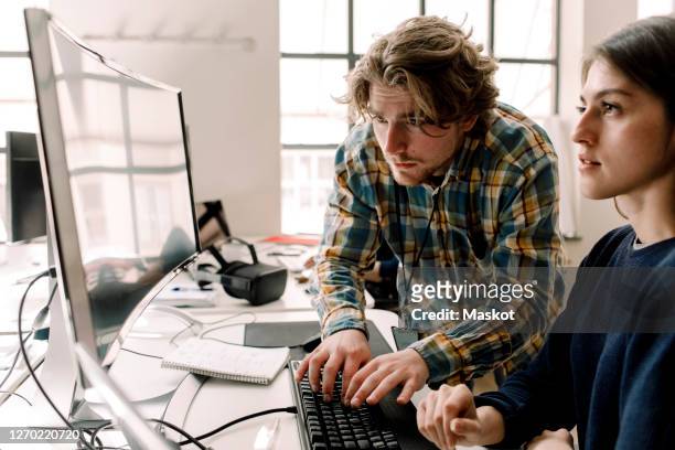 businessman typing while coworker looking at computer in office - iemand een plezier doen stockfoto's en -beelden