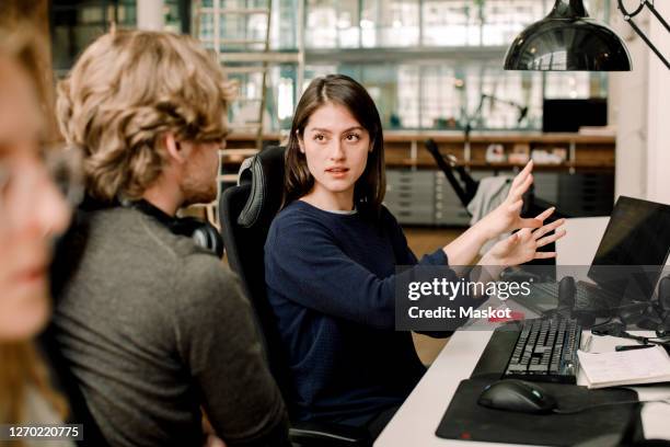 entrepreneur explaining to colleague while sitting in office - speaking explaining young woman stock pictures, royalty-free photos & images