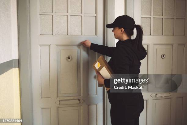 side view of delivery woman with package knocking at door - knocking on door stock-fotos und bilder