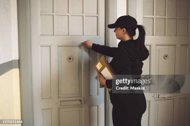 side view of delivery woman with package knocking at door - knock stock pictures, royalty-free photos & images