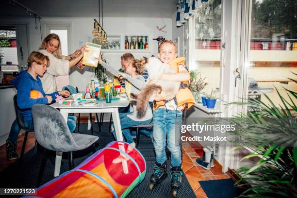 portrait of smiling boy with cat while family eating breakfast at table - breakfast family stock-fotos und bilder