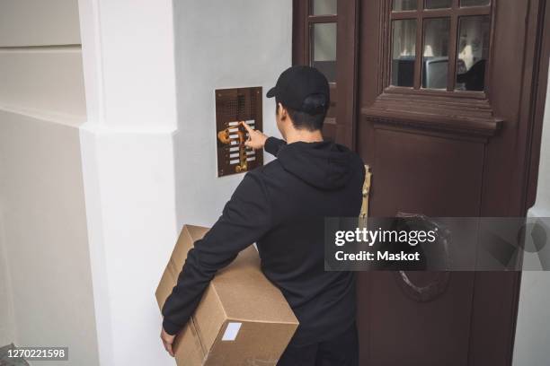 rear view of delivery man ringing bell at doorstep - door bell stock-fotos und bilder