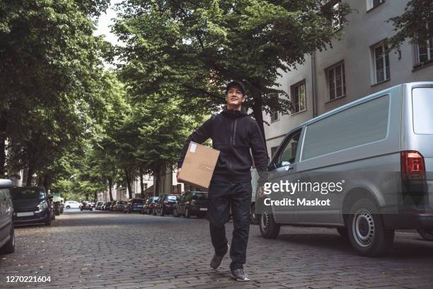 confident delivery man with package walking on street in city - courier stockfoto's en -beelden