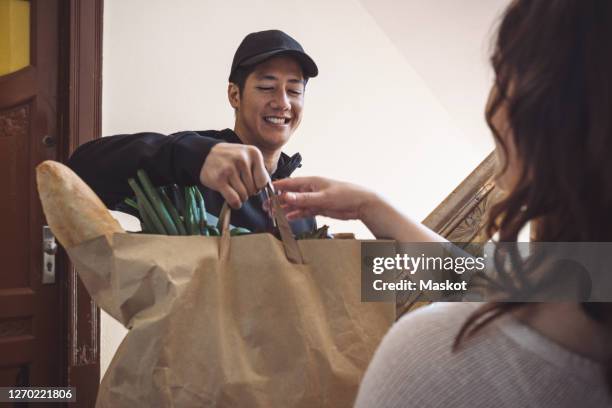 smiling delivery man delivering vegetables to customer while talking at doorstep - food delivery stockfoto's en -beelden