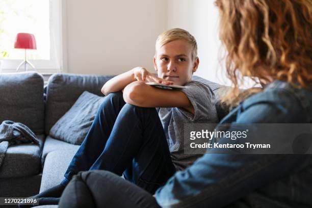 son talking to mother while sitting at home - zoon stockfoto's en -beelden