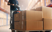 Shipment boxes, Cargo warehouse. Warehouse worker driving electric forklift pallet jack unloading pallet goods.