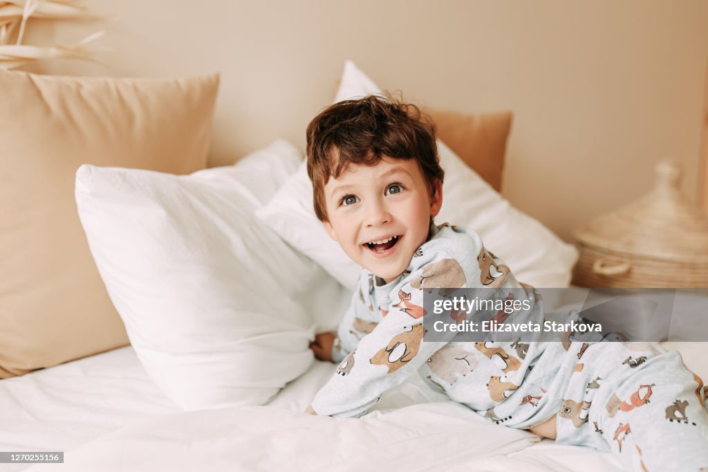 Cheerful child in pajamas laughs and has fun on the bed in a cozy home