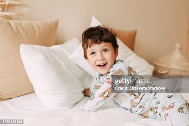 cheerful child in pajamas laughs and has fun on the bed in a cozy home - sleeping boys stockfoto's en -beelden