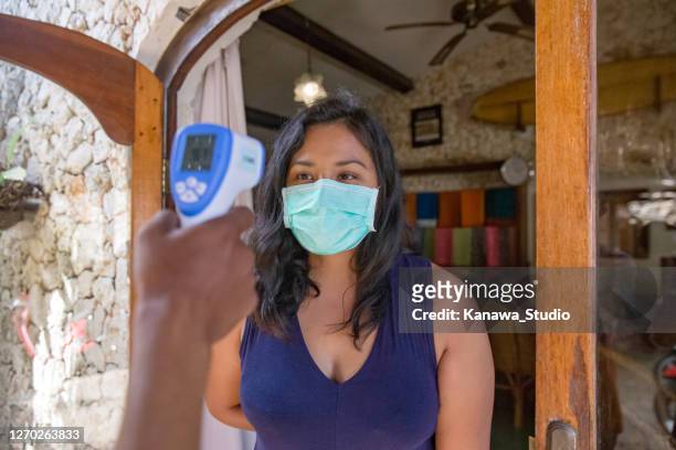 malaysische touristin, die ihre körpertemperatur vor dem betreten eines ladens im urlaubsort überprüfen lassen - fieberkontrolle stock-fotos und bilder