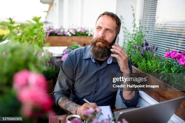 mature man with smartphone and laptop working on balcony, home office concept. - business smartphone happy spring fotografías e imágenes de stock