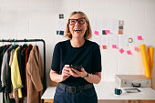 Laughing Mature Businesswoman With Mobile Phone In Front Of Desk In Start Up Fashion Business