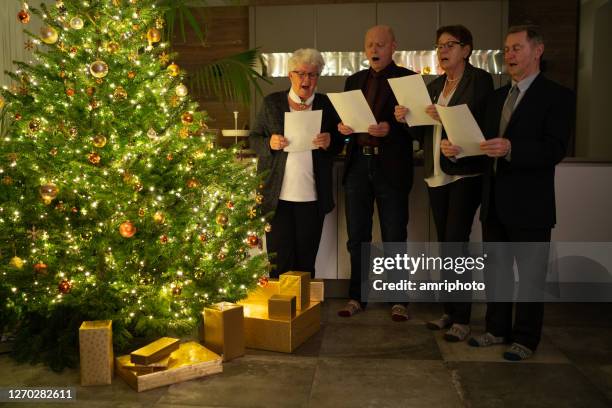 anziani cantando canti natalizi a natale albero a casa - christmas carols foto e immagini stock