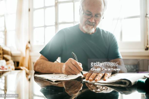 cropped image of senior men writing crossword on newspaper - kreuzworträtsel stock-fotos und bilder