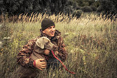 Hunter man with hunting dog Weimaraner in tall grass in rural field during hunting season