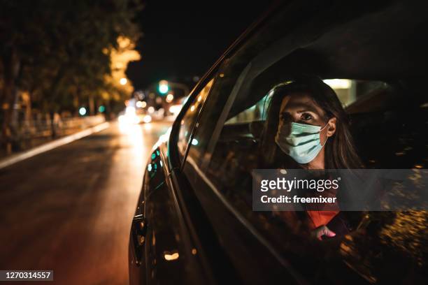 woman wearing face mask sitting on back seat and looking through window - taxi stock pictures, royalty-free photos & images