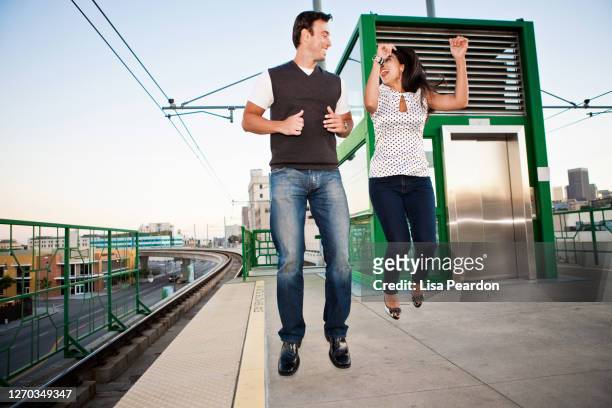 couple waiting for train jumping in thr air. - man woman train station stockfoto's en -beelden