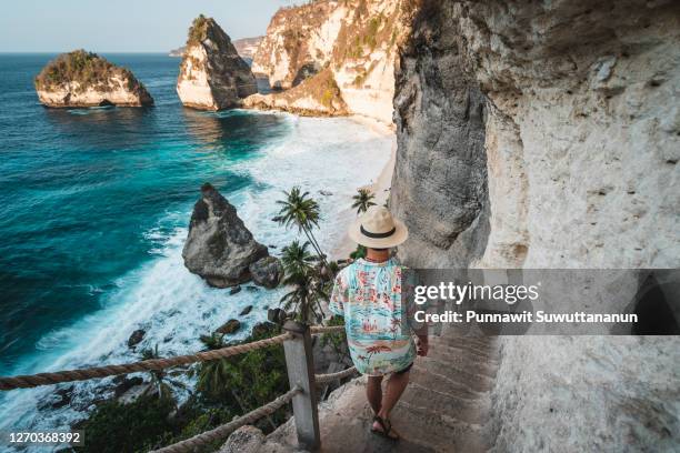 young asian traveller walking down to diamond beach in a morning sunrise in summer season. nusa penida island near bali island, indonesia - bali stock-fotos und bilder