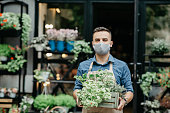 Small business and start of working day. Man in protective mask takes out box of plants outside
