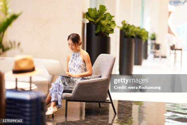 women lifestyle young asian tourist woman sitting on lounge chair hotel lobby using laptop working - wisdom knowledge modern stock-fotos und bilder