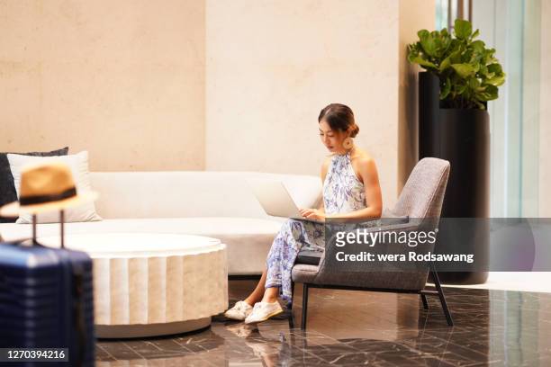 women lifestyle young asian tourist woman sitting on lounge chair hotel lobby using laptop - woman elegant crossed legs stock pictures, royalty-free photos & images