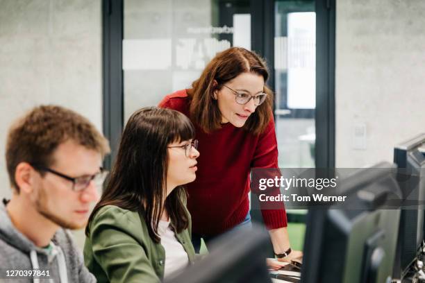 teacher helping student with computer work - mature coach fotografías e imágenes de stock